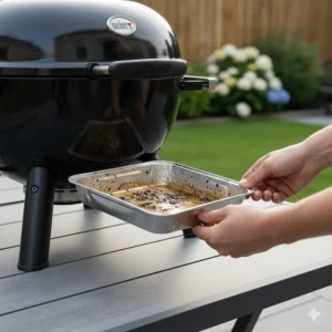 A hand removing the disposable drip tray from a Weber Q series BBQ for easy cleaning after a family roast.