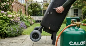 A portable gas smoker featuring side handles and sturdy wheels for easy storage in a British garden shed.
