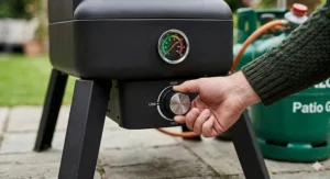 Close-up of an adjustable gas control knob and built-in thermometer on an affordable propane smoker.