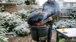 A detailed photorealistic 4K image showing a person in a waxed cotton jacket lifting a brisket from a smoking small kamado grill in a snowy British garden with a frosted glass of pale ale.