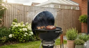 A classic black kettle-style charcoal barbeque being used as a smoker in a small suburban garden.