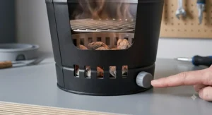 A detailed close-up of a finger adjusting the air vent control knob on a black bucket charcoal BBQ.