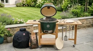 A detailed display of the kamado BBQ bundle contents, including the ceramic grill, heavy-duty cover, and essential cooking tools on a stone patio.