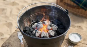 Close-up view of charcoal briquettes igniting inside a bucket charcoal BBQ with sparks and smoke.