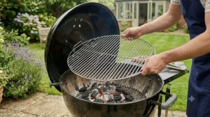 A man lowering a stainless steel cooking grate onto a black kettle barbecue over a bed of lit charcoal.