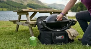 A portable gas BBQ fitting neatly into the boot of a car alongside other camping gear like a tent and a cool box, ready for a weekend trip.