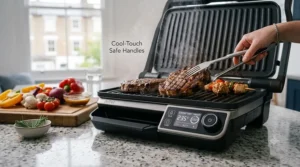 A safety-focused shot of an indoor barbecue on a granite worktop, featuring the text overlay Cool-Touch Safe Handles pointing to the device's handle while it is actively grilling.