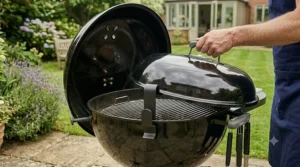 A man’s hand placing the lid of a kettle barbecue onto the integrated side hook, keeping it secure and accessible during grilling.