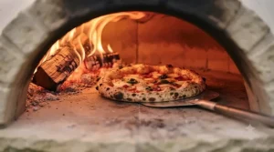 Artisan sourdough pizza baking on a glowing hot stone inside a traditional wood-fired oven.