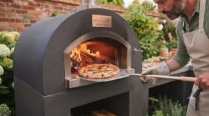 Artisan sourdough pizza being cooked on the stone floor of a hot built-in wood-fired pizza oven using a peel.
