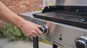 A close-up of a hand turning the control dial on a stainless steel gas BBQ to ignite the burners.