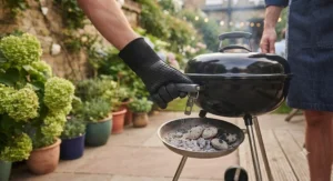 A person cleaning a removable charcoal ash tray from a barbecue priced under £200.