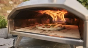 Rolling amber flames inside a portable gas pizza oven cooking a fresh Neapolitan-style pizza.