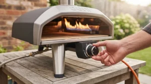 A person adjusting the dial on a stainless steel gas pizza oven on an outdoor patio table.
