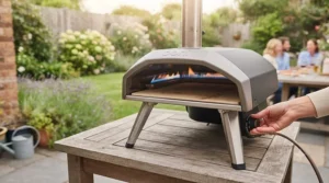 A compact, portable gas pizza oven set up on a wooden garden table ready for alfresco dining.