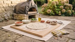 Homemade pizza dough stretched out on a wooden preparation board with fresh toppings.