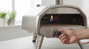 A close-up showing the secure attachment of a gas hose and clip-on regulator to a portable gas pizza oven for UK cylinders.