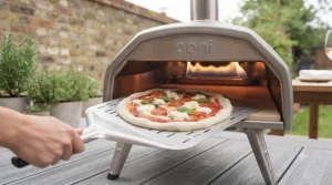 Looking inside the wide opening of a portable gas pizza oven to monitor the rising crust and bubbling cheese.