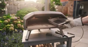 Removing and emptying the ash collection tray of a dual fuel pizza oven after wood-fired cooking.