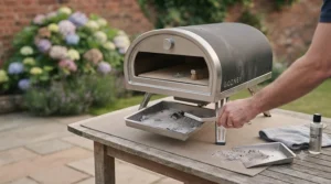 Emptying the cooled ash tray from a portable charcoal pizza oven as part of routine maintenance.