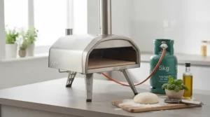 A portable gas pizza oven laid out alongside essential cooking gear like a peel, turning peel, and infrared thermometer.