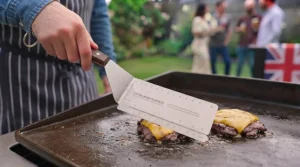 A wide spatula for burgers hanging on a kitchen rack by its integrated storage loop