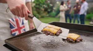 A wide spatula for burgers easily lifting two beef patties simultaneously on a flat-top grill