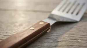 Close-up of an ergonomic wooden handle on a durable barbecue fish turner